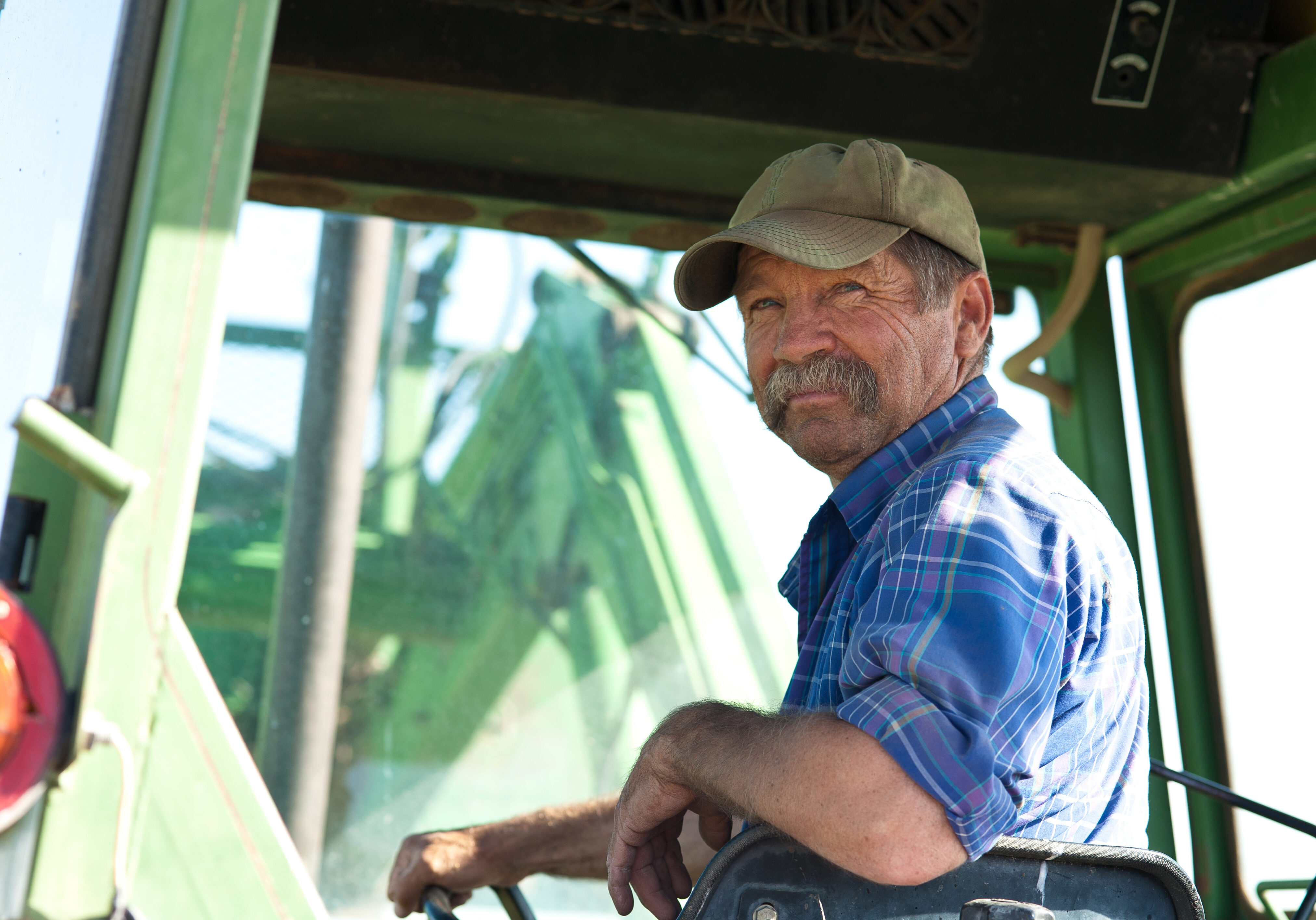 A candid portrait of a senior male farmer sitting in a tractor.